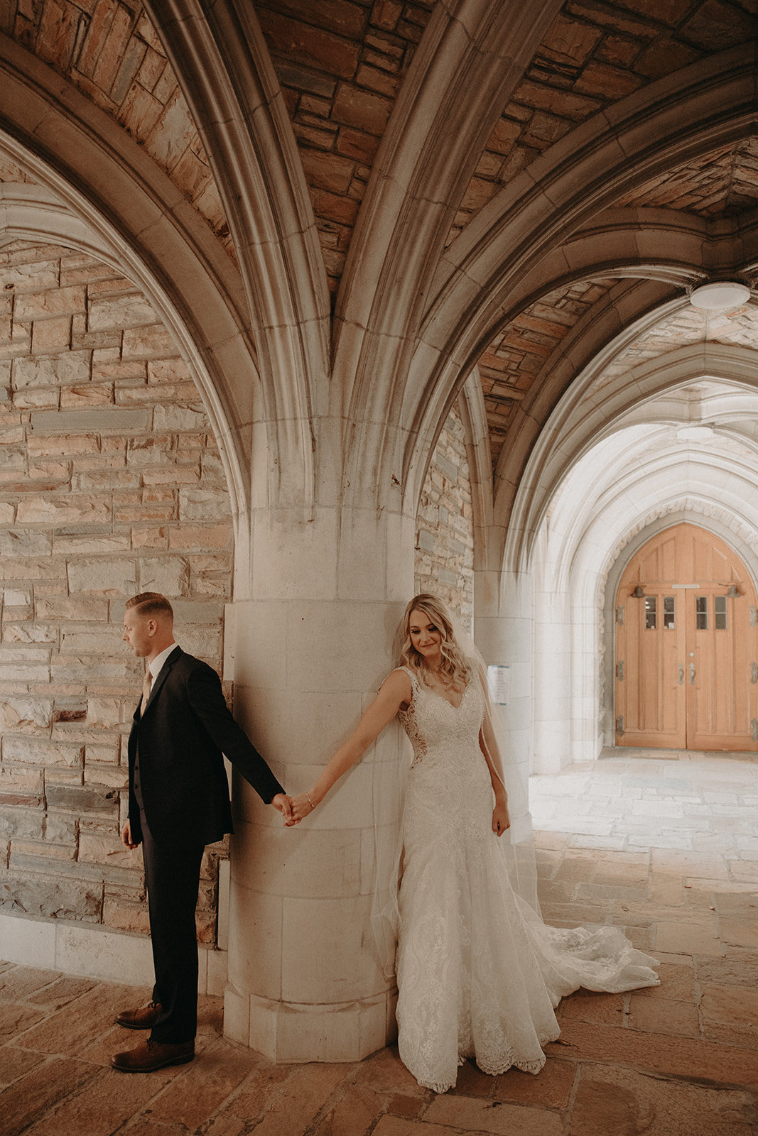 Couple holding hands during first look under the archway