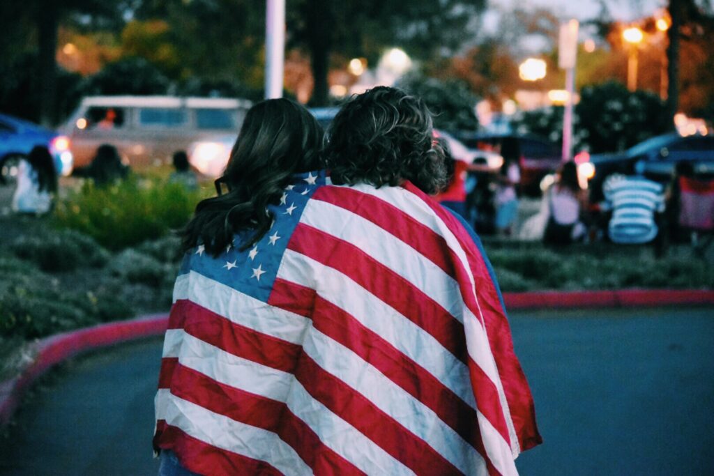 Two women embrace while draped in the American flag