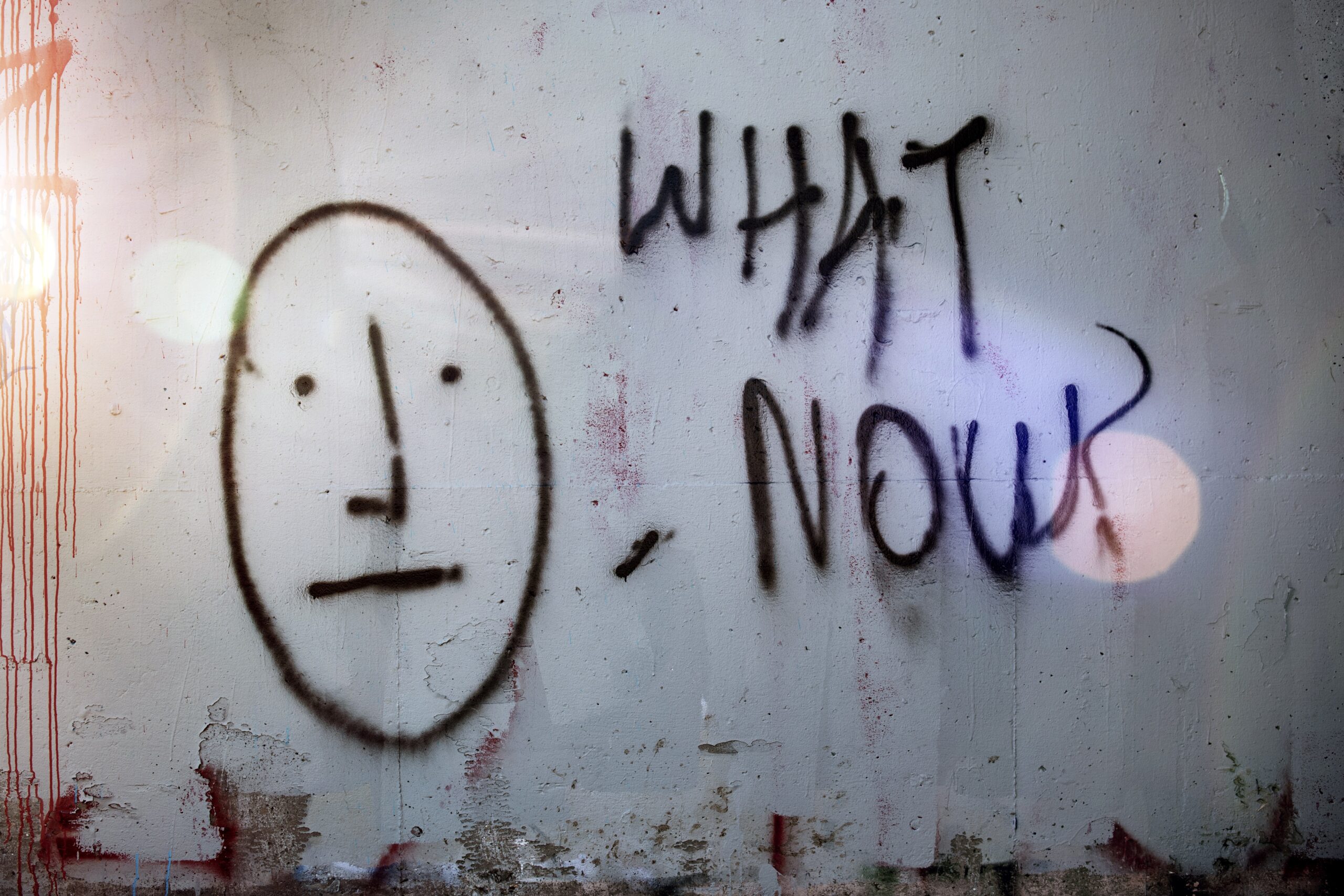 Graffiti on wall that reads, "What now?"